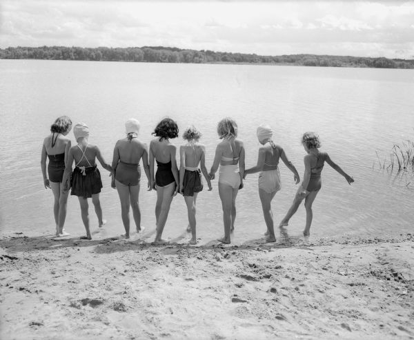 A group of nine girls test the water of Lake Wingra prior to beginning a swimming lesson.