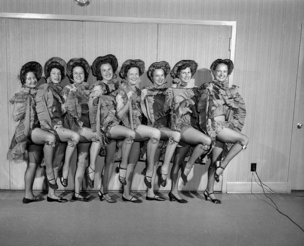 Eight chorus cancan dancers high-kicking at the Blackhawk Country Club Gay 90's party.  Left to right: Ellsworth Mack, Dorothy Bleecker, Lois Blau, Martha Reynolds, Elizabeth Geisler, Alzeda McCormick, Elizabeth Maloof, and Faye Nelson.