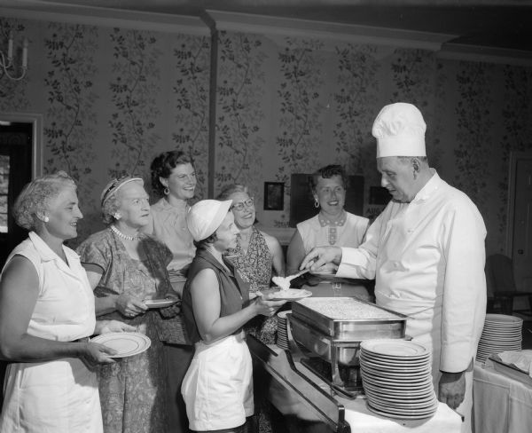 Chef Jean Williams serving a buffet lunch at the Maple Bluff Country Club during the women's inter-club golf match. Ladies being served are Virginia Keliher, Tessie Hackworthy, Stella Steinhauer, Frances Sanford, Dorothy Steiro, and Marion Leifer.