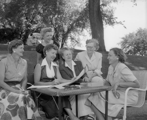 Six women gathered around a table at the Maple Bluff Country Club during the women's inter-club golf match. Seated, left to right, are: Ruth Rasmussen of Nakoma, Helen Svendsen of Maple Bluff, Lucille Kimball of Blackhawk, Bess Smith of Blackhawk, and Muriel Campbell of Maple Bluff. Standing is Lela Stuben of Nakoma.