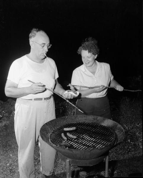 William and Audrey Hobbins cooking a hot dog on the grill at the Mendota Yacht Club beachcombers party.