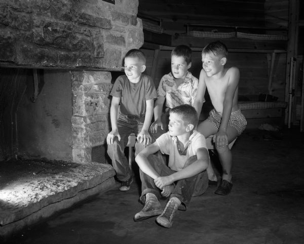 Fritz Ragatz (foreground) and (from left) Billy Garrott, Frank Kellogg, and Jack Kendall sitting in front of the fireplace in one of the cabins at YMCA's Camp Wakanda on Lake Mendota during a rainstorm.