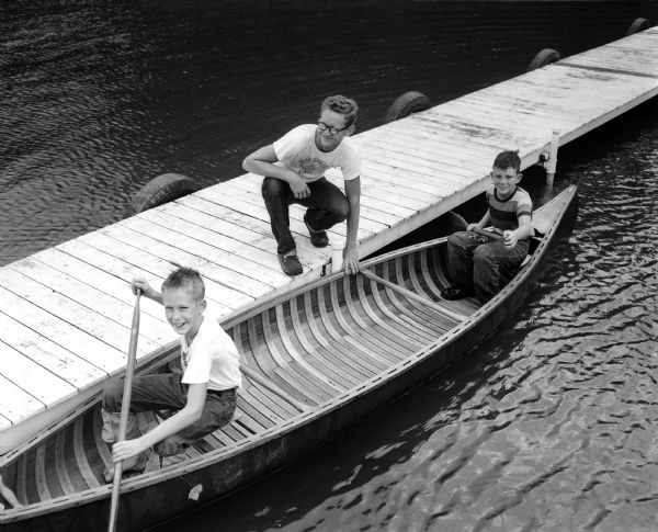 A scene at YMCA's day camp at Camp Wakanda, located on a shore of Lake Mendota. Counselor Rick Dettloff, standing on a pier, steadies a canoe for Jerry Hannifan, left, and Jay Hintz.