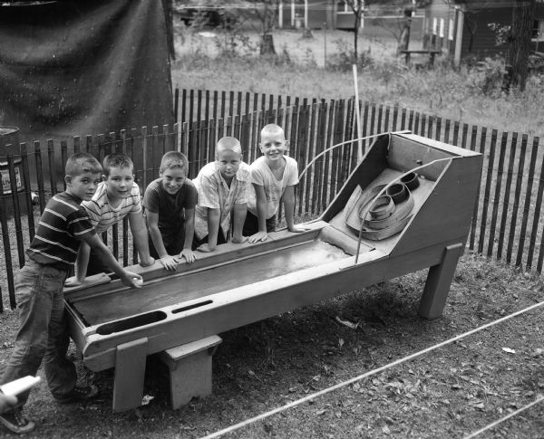 A scene at YWCA's day camp at Camp Wakanda, located on a shore of Lake Mendota. Five boys play a Skee ball game on "Carnival Night." Left to right: Michael Maloney, Joe Southworth, Larry Shapiro, Richard Wilkinson and John Vick.