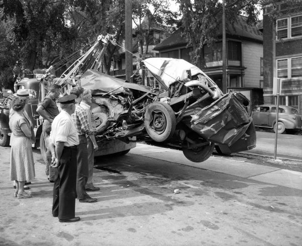 A group of Madison residents view the twisted hulk of a car in which David Huse, an airman at Truax Field, was killed. The accident occurred 4 miles south of Sauk City on Highway 12-13 in the town of Roxbury.