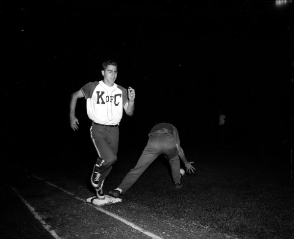 A softball base runner wearing a "K of C" softball jersey touches base before the Shriner baseman can scoop up the softball.