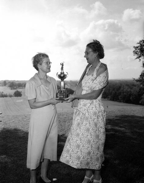 Eleanor Persons and Lydia Shafer, Blackhawk Women Golfers, posing for a portrait outdoors with a trophy.