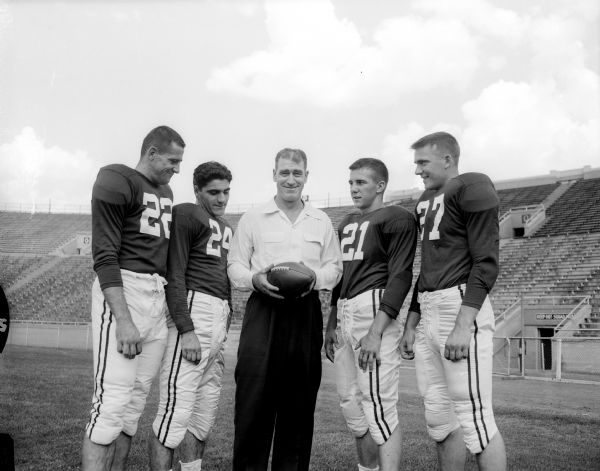 University of Wisconsin head football coach Ivan Williamson poses with four candidates for quarterback of the 1953 football team. The players are, from left: Glen "Buzz" Wilson of Milwaukee, Gust Vergetis of Milwaukee, Jim Miller of Eau Claire, and Jack Stellick of LaCrosse.