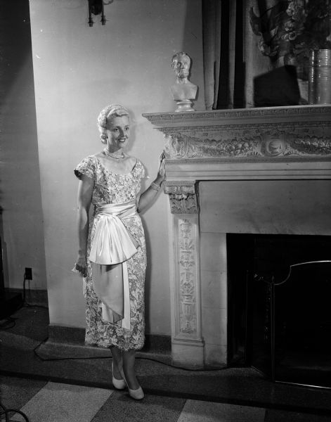 Lillian Honeck, wife of the Deputy Attorney General of Wisconsin, poses beside a fireplace. She is a model in the Zonta Style Show.
