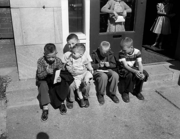 Four third grade boys are shown sitting on the steps outside St. Patrick's School, located at  630 East Washington Avenue, on the first day of school. The boys are, from left: Dennis O'Connell, Allan Curriell, Allan's younger brother Jeffrey Mark Curriell, James Kennedy, and John Wecker. They were a part of 3,000 enrollees in Madison's nine Catholic schools.