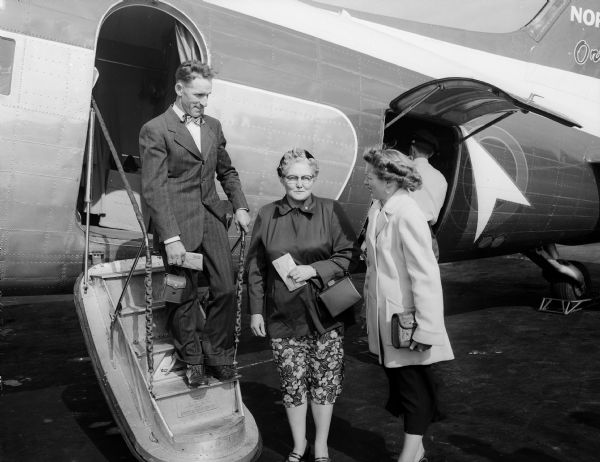 Mr. and Mrs. Garrett Turner, Richland Center farmers, stand by the steps of a Northwest Orient airliner with their daughter, Mrs. Chester Hall. The Turners were going to San Francisco to greet their returning P.O.W. son, Sargeant Wilford W. Turner.