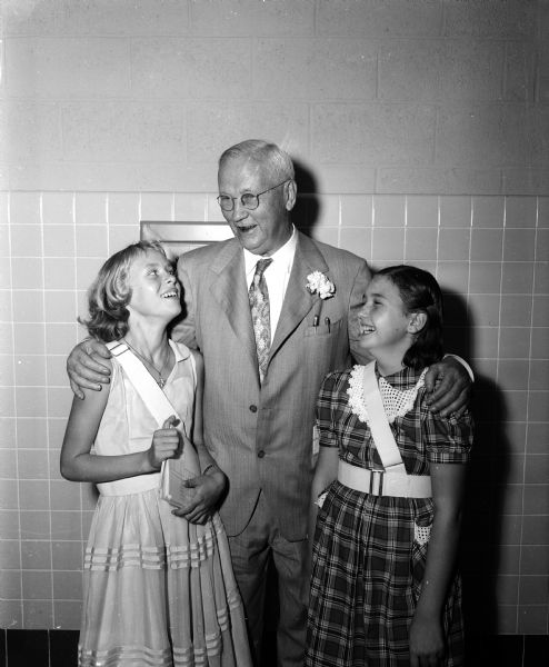 Herbert C. Schenk and two sixth grade students greet each other at the dedication of the new grade school named for Schenk. The two girls, both wearing school crossing guard belted sashes, are Vicki Briggs and Kay Lynaugh. The school is located at 230 Schenk Street near Milwaukee Street.