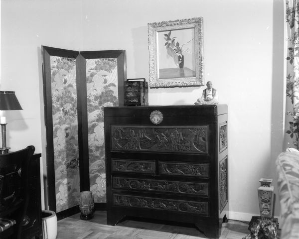 The W.H. Wikoff residence, 34C University Houses, contains many Japanese furnishings. A hand-carved Japanese chest is shown with a teakwood sweetmeat box and a Hakata doll. There is a screen made of silk obis and a Japanese urn on a highly polished tree root stand. Above is a painting by Mrs. Wikoff.