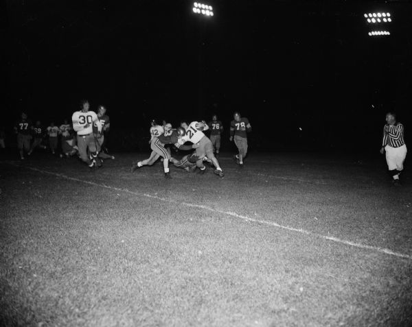 Action shot of Central High School left halfback ball carrier Jim Easland (#21) being tackled by East High School's Don Shillinglaw (#33) and Dick Barton. Central High School won with a score of 19-0.