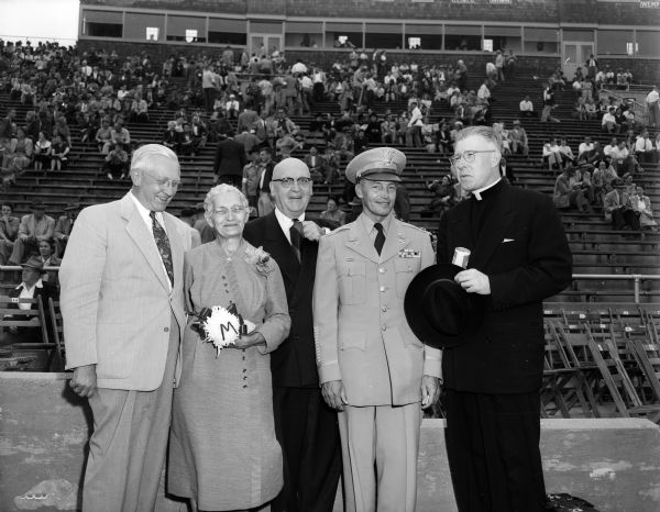 Former P.O.W. George R. Hansen posing for a photograph after a football game between Wisconsin and Marquette at Camp Randall. The game climaxed a day of honors from area city and civic groups. Left to right: Former Governor Oscar Rennebohm; Mrs. Hansen (mother of George); U.W. President E.B Fred; Colonel Hansen; the Very Reverend Edward J. O'Donnell, S.J., President of Marquette University.