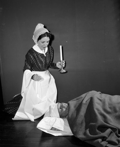 Depicting Florence Nightingale at the time of the Crimean war of 1853, a costumed Marie Timlin tends to "wounded soldier" Harold Hermanson. The enactment is an activity during National Business Women's Week which is being observed with special features in the press, radio, and television stations to show the progress which women have made through the years. The project is sponsored by the Madison Business Women's and Professional Women's organizations.