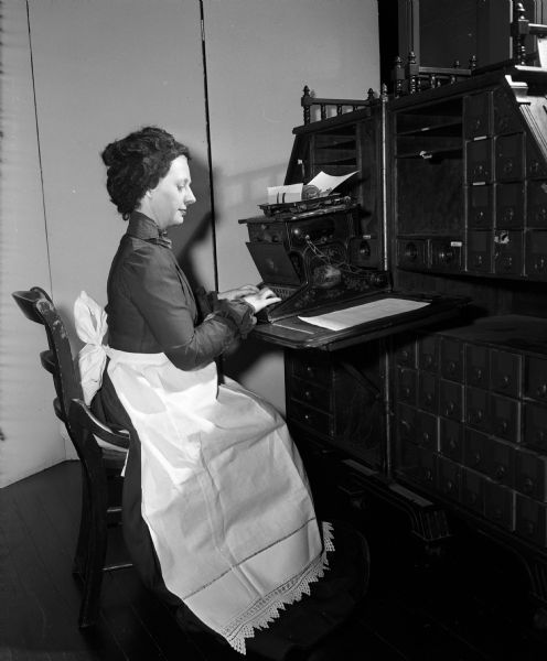 Ardis Kirkpatrick, a private secretary to Wisconsin Supreme Court Justice Grover Broadfoot, is wearing the costume of an 1800's typist while using a Sholes and Glidden typewriter of 1878. The enactment is an activity during National Business Women's Week which is being observed with special features in the press, radio, and television stations to show the progress which women have made through the years. The project is sponsored by the Madison Business Women's and Professional Women's organizations.