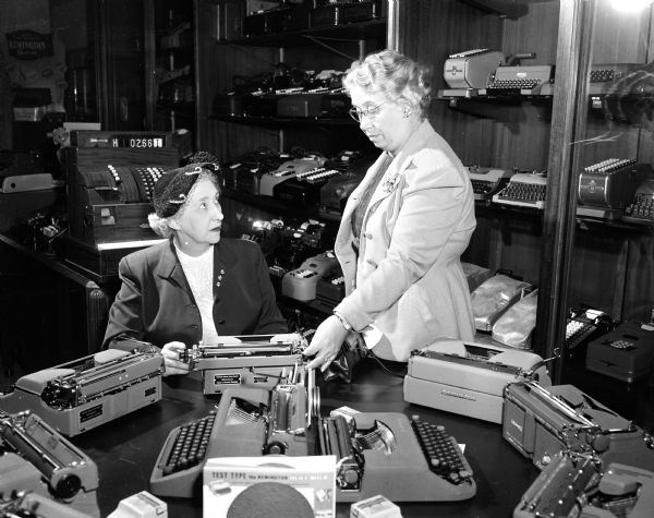 Elizabeth Stemp (right), owner of the Stemp Typewriter Company, shows a typewriter to  customer Mildred Subey, associated with the Herfurth Insurance Agency. Elizabeth represents the contemporary business women as an activity during National Business Women's Week which is being observed with special features in the press, radio, and television stations to show the progress which women have made through the years. The project is sponsored by the Madison Business Women's and Professional Women's organizations.