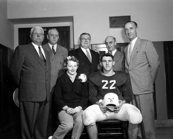 Group portrait of the dignitaries who participated in Sun Prairie's dual celebration of Homecoming and the official dedication of Ashley Field, the new high school athletic field. Seated in the front row are the Homecoming queen, Mary Derr, and Homecoming king Harold Parr. Behind them (from left) are: Dr. James Weigen, R.F. Schiller, Charles Ashley, Leo Brandenstein, and C.E. Wetmore. Weigen, Schiller, and Brandenstein are members of the Sun Prairie school board; Wetmore is superintendent of schools; Ashley is the Sun Prairie H.S. alumnae who donated the land for the athletic field.