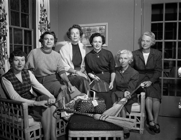 Group portrait of committee members who are making arrangements for annual tea and sale sponsored by the Madison alumnae of Pi Beta Phi sorority, at the chapter house, 133 Langdon Street. They are, from left:  Jane (Mrs. Kenneth) White; Barbara (Mrs. John R.) Shaw; Mary G. (Mrs. Robert W.) Ela; Emma (Mrs. C. Harvey) Sorum; Dorothy (Mrs. Richard E.) Ela; Lucille (Mrs. Eugene P.) Connor. Sale products made by mountaineer people near Gatlinburg, Tennessee are displayed.