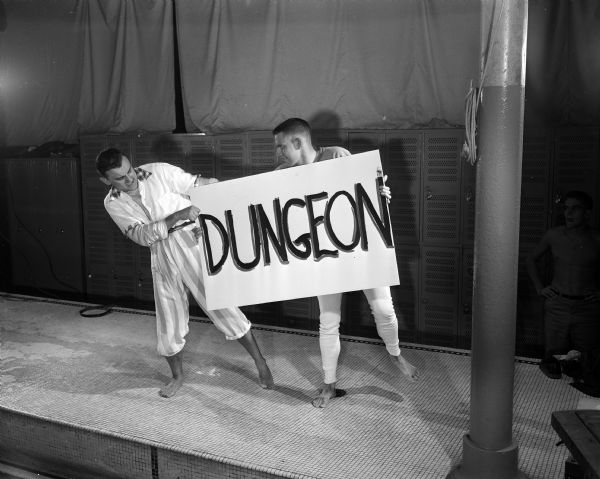 During a scene from the UW Men's Dolphin Club show "Robin Hood Comes Clean," Don Hart of Whitefish Bay holds a sign with the word "Dungeon" written in large letters. At left is Arlie Schardt, Milwaukee, director and narrator for the show.