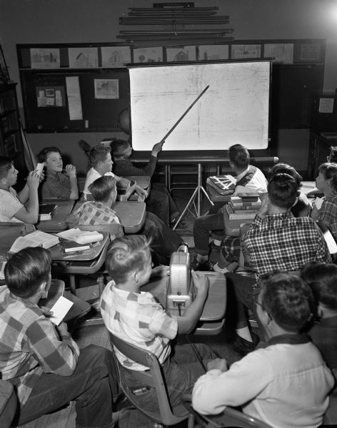 The Nichols School fifth grade class looks at a filmstrip created by Visual Education Consultants. The screen shows a picture of the scale model of the original Nichols School created by the students and published in the <i>Wisconsin State Journal</i> on Oct. 22, 1953.