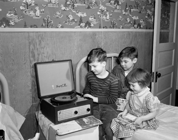 Three children at the Morningside Sanatorium listen to a phonograph record being played on a record player purchased with money from the sale of Christmas seals by the Madison Tuberculosis Association.