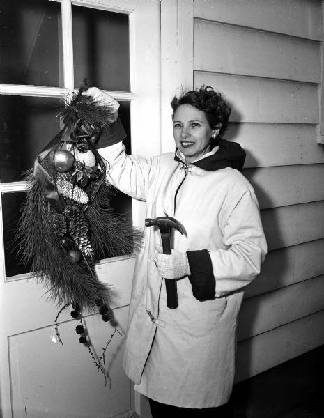 Maybelle Otterson demonstrates a Christmas custom as she hangs a front door decoration on her home at 209 North Blackhawk Avenue in Shorewood.