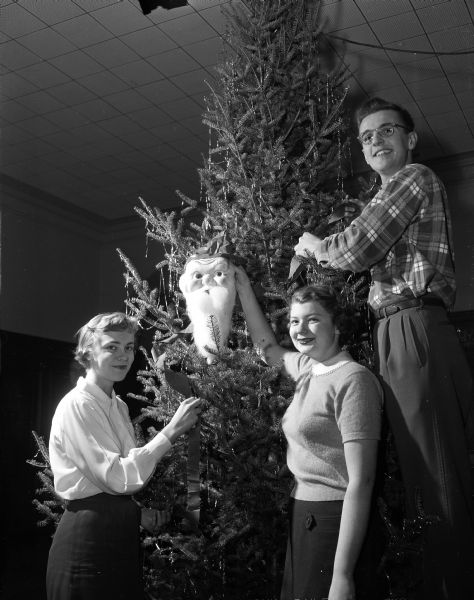 West High School students Janis Tande, Phyllis Waddell, and Dick Stephen decorate a Christmas tree for a school party.