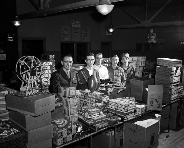 Group portrait of five men working at the Empty Stocking Club Toy Depot. Left to right: Captain Leo Lewis, U.S. Marine Corps; James L. Williams and William K. Kuntz, Dane County Department of Public Assistance; Sargent Cris Krabbe, U.S. Marine Corps, and Officer Melford C. Burkeland, U.S. Marine Corps.