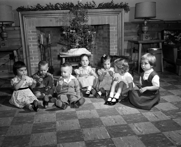 Seven small children are shown enjoying cookies while seated on the floor in front of a fireplace at the new interns and residents' quarters. The Christmas party was sponsored by the Interns and Residents Wive's Club of University Hospitals. The children, shown left to right, are: Christy Russo, Donnie Korst, Danny Foe, Pamela Albin, Debbie Albin, Betsy Bolden, and Janie Kiekhofer.