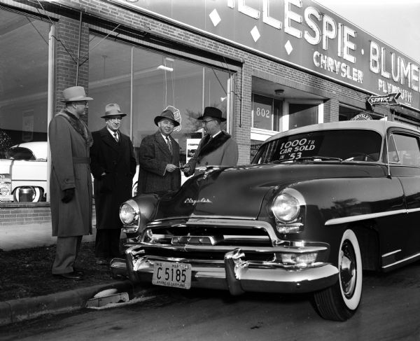 Lester J. Blumer (right), treasurer of Gillespie-Blumer Motors, Inc., gives the keys of a 1954 Chrysler Windsor to Harold W. Herne. Mr. Herne is purchasing the 1000th car sold at by Gillespie-Blumer in 1953. Looking on is C.L. Duquaine (left), general manager, and J.P. Gillespie, president and founder of the company. Gillespie-Blumer is located at 802-802 East Washington Avenue.