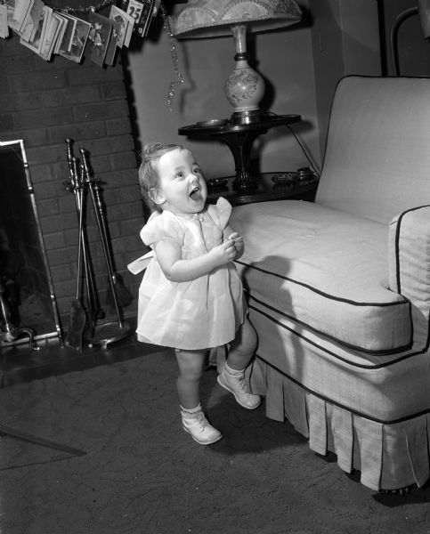 Mary Jo Sweeney standing next to a couch. The photograph was one of a series featuring the children born one year ago on New Year's Day of 1953.