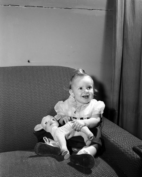 Joanne Butler holding a stuffed lamb. The photograph is one of a series featuring the children born one year ago on New Year's Day of 1953.