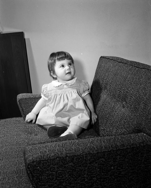 Portrait of Marcia Ann Mender sitting in an easy chair. The photograph was one of a series featuring the children born one year ago on New Year's Day of 1953.