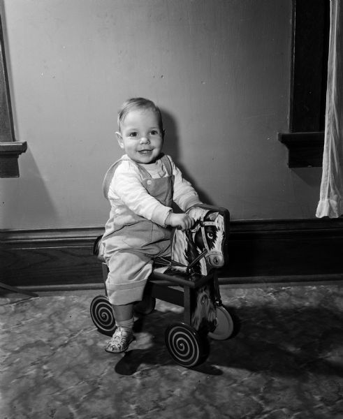 Portrait of Dennis McCarthy riding a toy horse. The photograph was one of a series featuring the children born one year ago on New Year's Day of 1953.