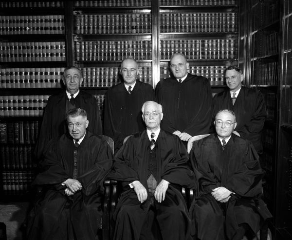 Group portrait of the members of the Wisconsin Supreme Court. Standing left to right: Justices Edward Gehl, George R. Currie, Roland J. Steinle and Timothy Brown. Seated: Justice John E. Martin, Chief Justice Edward T. Fairchild, and Justice Grover Broadfeet. The photograph was taken in the court's conference room.