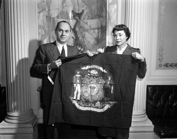 Governor and Mrs. Walter J. Kohler, Jr. holding a state flag requested for display by a Pacific Air Force hospital. Behind them some of the wall decorations near the Governor's office can be seen.