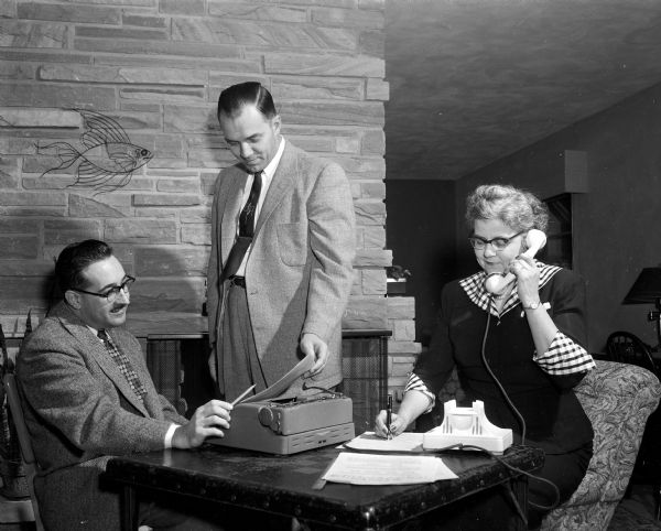 Officers of the Orchard Ridge Community Club working on the club's local newspaper. President James Motl, standing, submits an item to Glenn Lyans, vice-president and editor. On the telephone is secretary-treasurer Mrs. Carl (Frances) Crane.