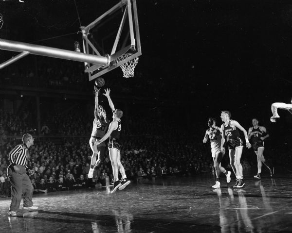 Action shot from the January 11, 1954 basketball game between the University of Wisconsin and Northwestern. Wisconsin's Bob Weber (#50) drives a lay-up over the blocking attempt of Northwestern's Walt Stoeppelwerth.