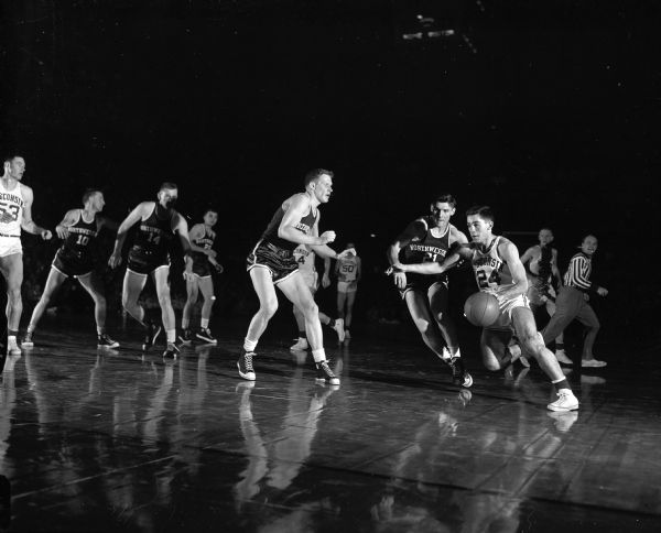 Action shot from the January 11, 1954 basketball game between University of Wisconsin and Northwestern. Wisconsin's Ron Weisner (#24) drives around Don Blaha of Northwestern (#21). Wisconsin's Dick Cable (#39) is seen in the background.