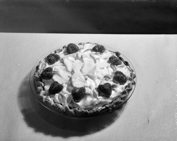 A recipe from Mrs. Anna Trinrud of Madison, St. Valentine's pie made with lemon meringue with bits of orange peel, sitting on a table. The pie is decorated with hearts.