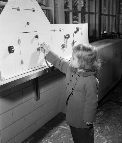 Patricia Thieding, daughter of Mr. and Mrs. Lawrence Thieding of Loganville, tries to unlock a door in a play item designed by Jean Hardenbergh from Lake Zurich, Illinois. It was one of many play items set up for the Farm and Home Week at the University of Wisconsin School of Home Economics.