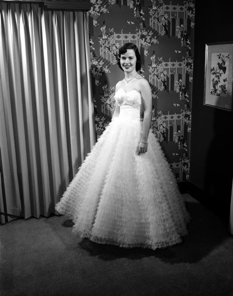 Portrait of Peggy Cafferty, University of Wisconsin Junior Prom queen finalist, wears a "ruffled white net strapless formal" with a full length skirt. She was one of six finalists for prom queen. The dancers later elected the queen on the night of the prom.