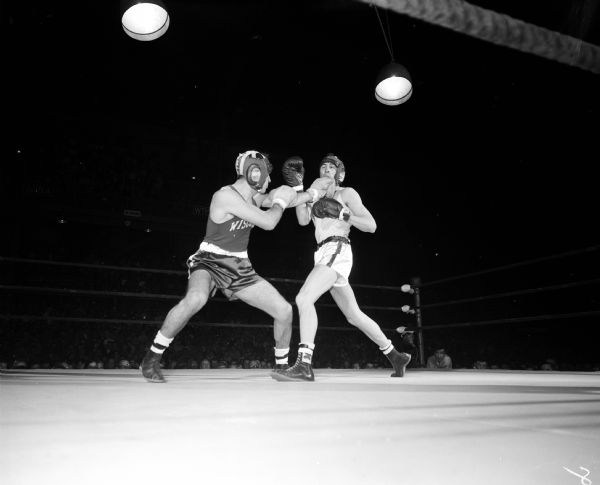 Dick Trainor of Madison (left) lands a left punch on his opponent, Everett (Butch) Chambers of Tomah, during the all-university boxing finals at the University of Wisconsin-Madison Field House. Trainor was crowned the 165-pound champion and winner of the "Fightinest Fighter" award. He left after his final bout to visit his father who collapsed of a heart attack during the second round and died later in a Madison hospital.