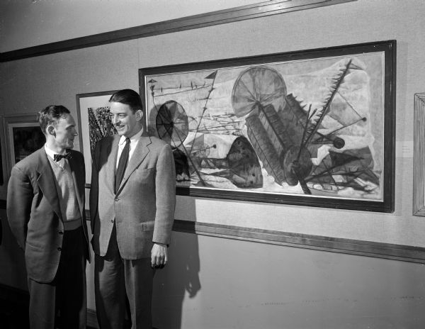 John Colt of Janesville and one of the jurors, Rainey Bennett of Chicago, are shown with Colt's oil painting, "Burial Ground." Colt received the Mrs. Frances M. Marschall award for this painting. It is marked in distinctive planes, mostly in greys.  Colt, a Wisconsin graduate, teaches in the Janesville Vocational school. The annual Madison Artists exhibition was held in Scanlan Hall.