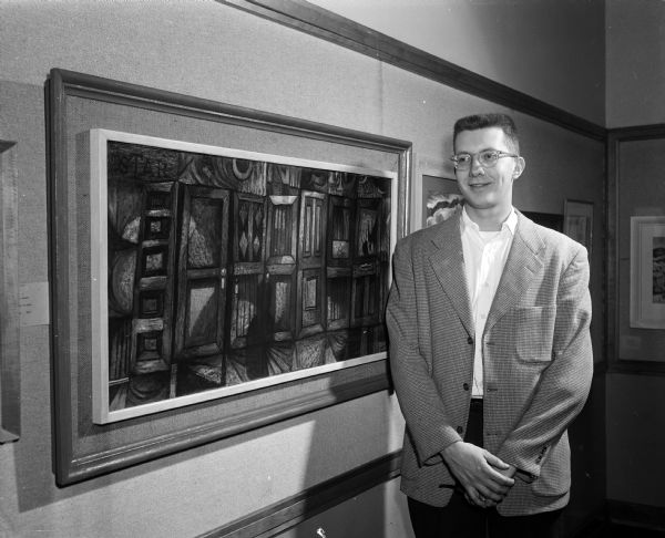 Bob Burkhert, a University graduate student from Racine, won the Mr. and Mrs. Joseph Ford award of $75 for his oil painting of "Wall of Doors." He stands beside his painting at the Madison Artists Exhibit at Scanlan Hall.