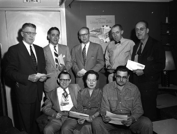 Group portrait of some of the Sears Roebuck employees in Madison who have long terms of service. They hold their statements of shares from the firm's profits. Standing, left to right, are: Store Manager Carl Van Peenen, George Schoen, Clifford Helbing, Ole Selje, and Walter Krause. Seated, left to right, are: Stanley Hagen, Ruth Staebler, and Les Daley.