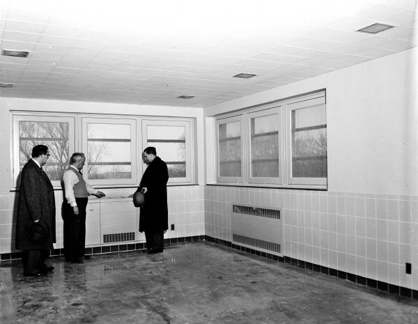 An interior view of the new Wisconsin Diagnostic Center for the intensive study of mentally and emotionally disturbed young people, referred to it by the state Department of Public Welfare. It is under the supervision of the Mental Hygiene Division of the State Department of Public Welfare and connected with the University of Wisconsin medical school as a training ground for medical students and future psychiatrists. Observing building details are Clarence Graham, business administrator of the State Division of Mental Hygiene in the Wisconsin Department of Public Welfare; building engineer Allen C. Small; and Dr. Leslie Osborn, Director of the Division.
