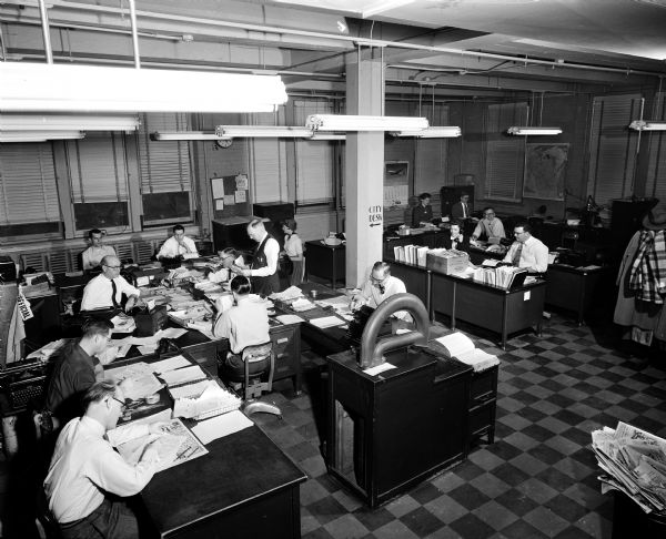 View of men and women working at desks in the editorial room of the Wisconsin State Journal newspaper.